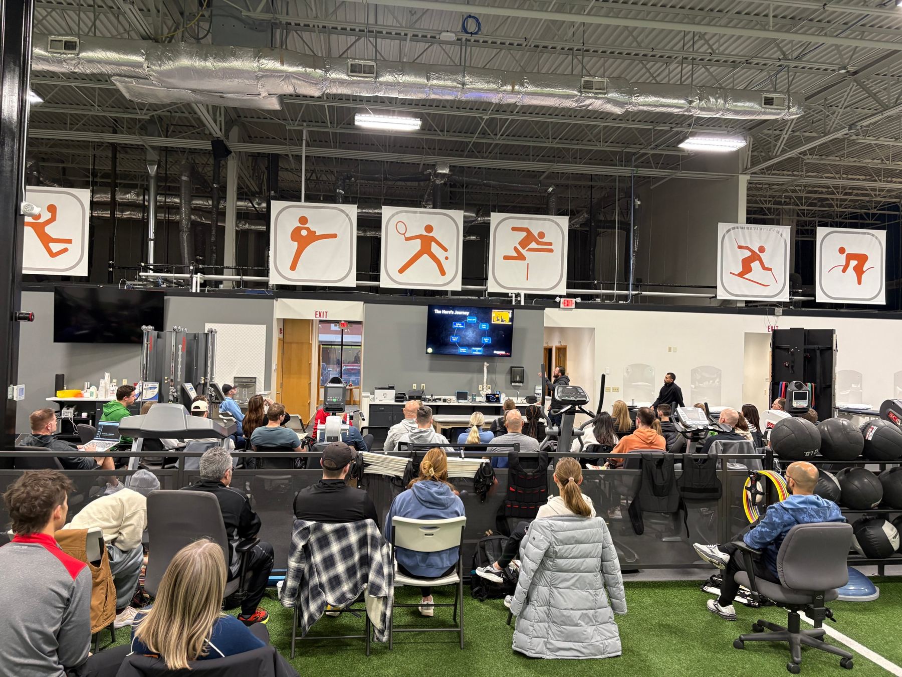 A full room of clinicians watching Chris present in a training facility